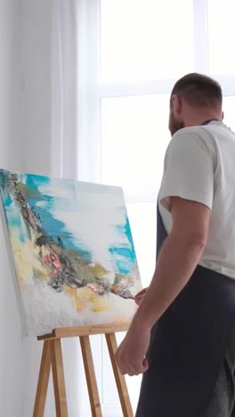 male artist paints a picture and dances in the studio