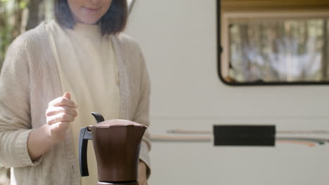 mujer sonriente haciendo café en la parrilla de barbacoa en el camping en el bosque