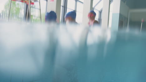 underwater shot of children jumping into indoor swimming pool from edge