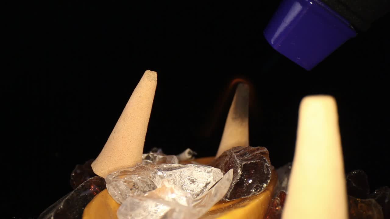 장식용 바위 정원에 있는 세 개의 향 콘, 작은 부탄 토치로 불이 붙은 콘을 뒤로 밀고 있습니다.