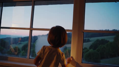 child looking out window at sunset