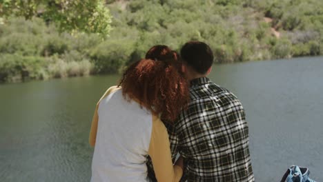 happy african american couple sitting on bench at lake in forest, slow motion