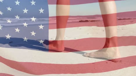 Animation-of-American-flag-waving-over-legs-of-woman-walking-on-beach-by-seaside