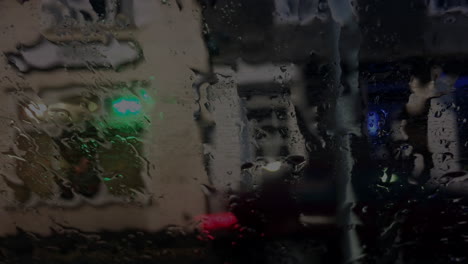 View-of-street-traffic-through-car-windscreen-at-night-when-raining,-static-shot