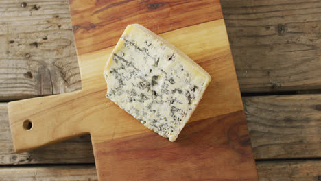 video de una toma aérea de una cuña de queso azul en una tabla de cortar, en una mesa de madera rústica