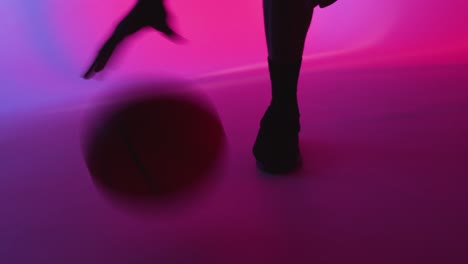 silueta de estudio de un jugador de baloncesto masculino driblando y rebotando la pelota contra un fondo iluminado de rosa y azul 3