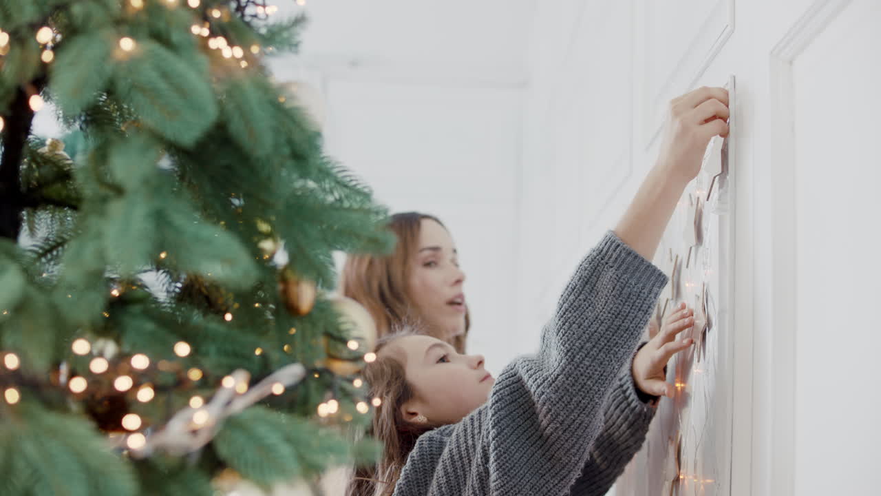 mujer sonriente abrazando a una chica cerca del árbol de navidad en la sala de estar.