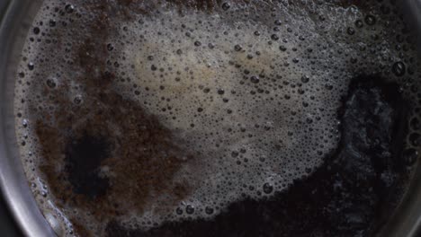 a top view close-up of tea boiling with a foamy surface and steam