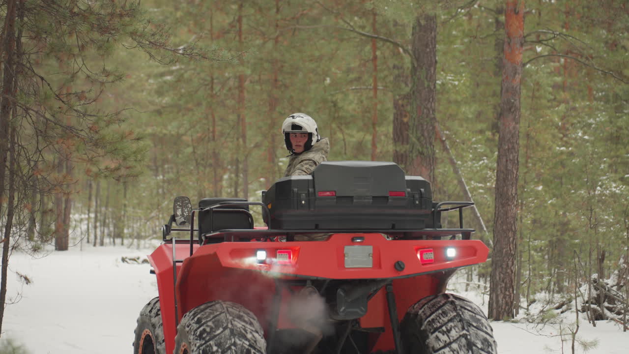 Quad rosso su sentiero innevato nella foresta, vista frontale con pilota in casco bianco in piedi, vapore dal motore e fari visibili, pneumatici che fanno presa sulla neve tra i pini, atmosfera di esplorazione costante, viaggio fuoristrada estremo.