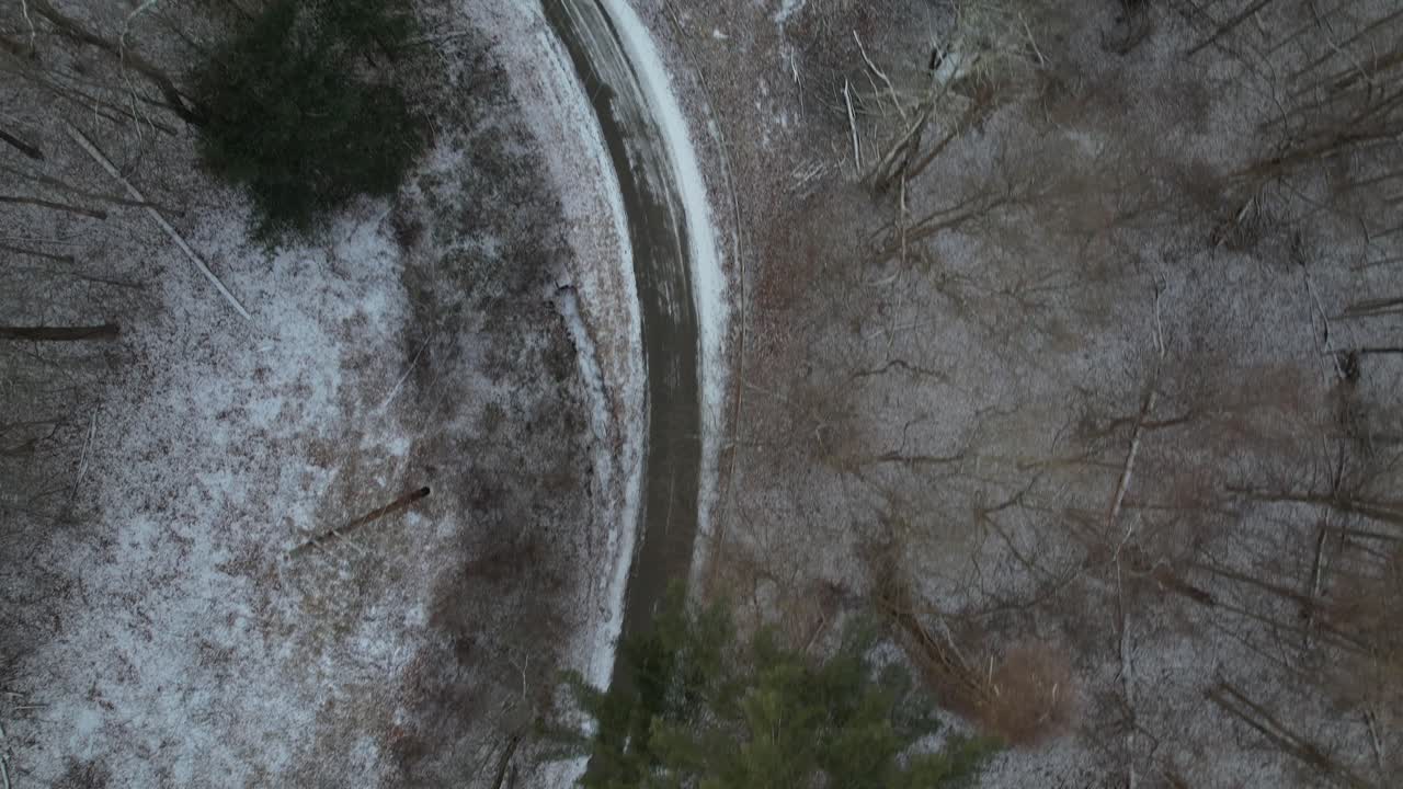 una vista de arriba hacia abajo directamente sobre un camino de tierra con nieve en el suelo y pinos altos