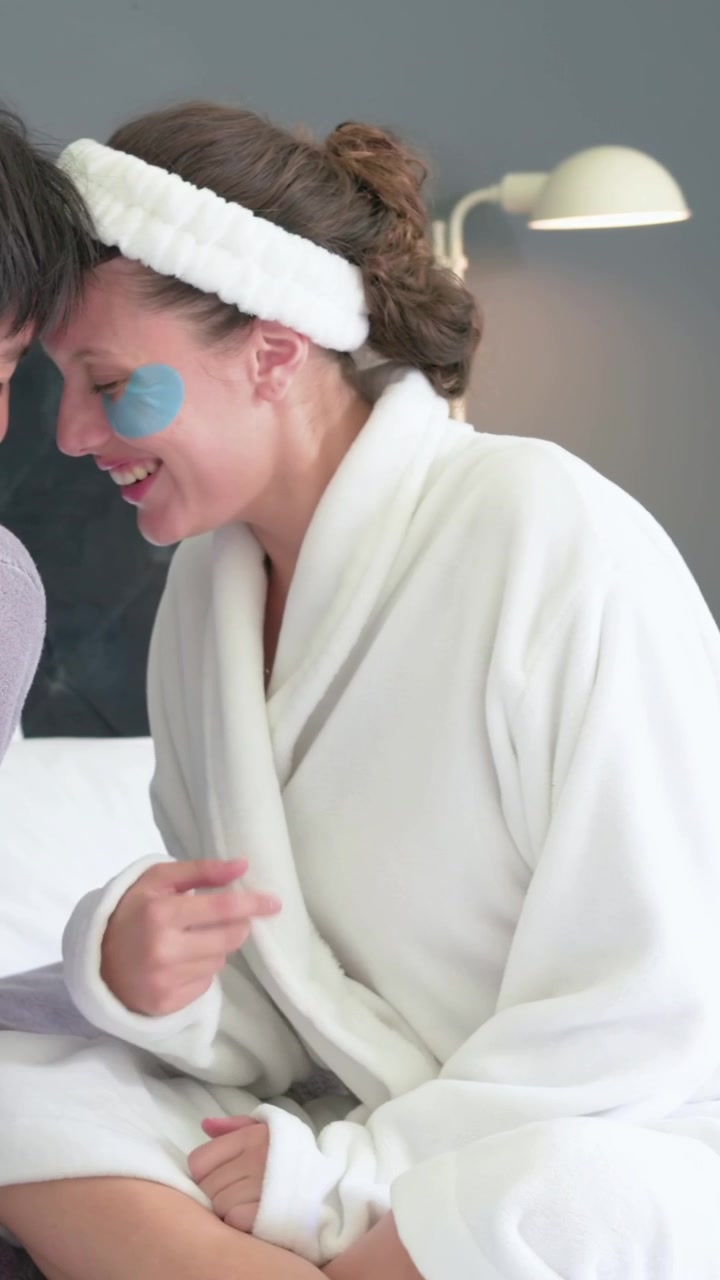 Vertical video: Panning camera showing pair leaning on bed wearing robes, blue patches for skincare