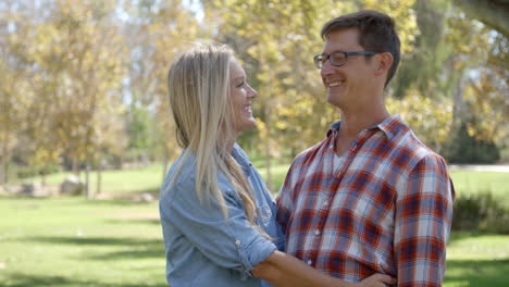 Caucasian-couple-embracing-in-a-park,-and-looking-to-camera