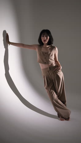 vertical video: model posing confidently in stylish beige outfit against studio backdrop