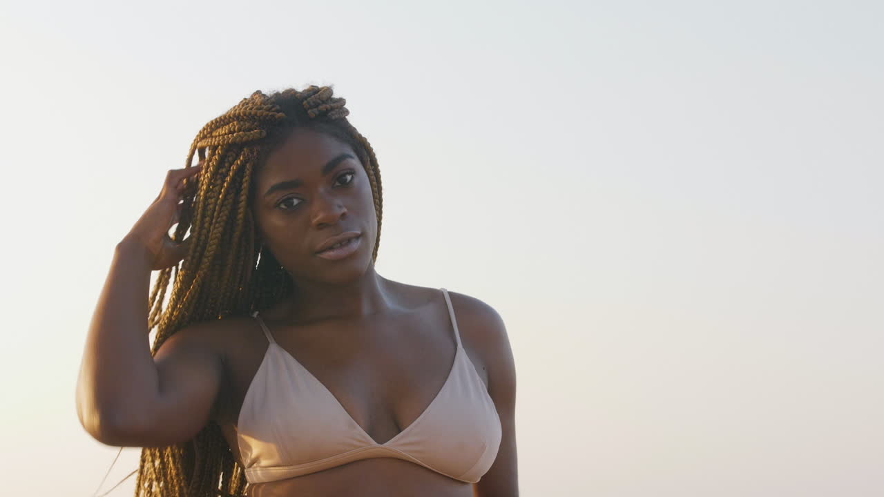 African swimwear model playing with her braids while posing in a bikini top