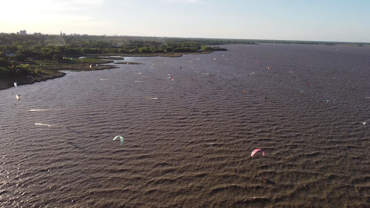 toma aérea de muchos kitesurfistas en el río al atardecer con destellos de sol en la lente
