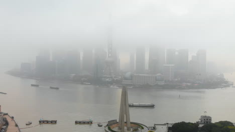 descending drone revealing the monument to the people's heroes and the busy waibaidu bridge on a dense foggy day