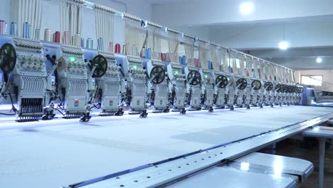 view along row of automatic fabric embroidery machines at garment factory in karachi