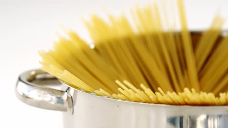 raw spaghetti arranged in silver container ready to be cooked on white background