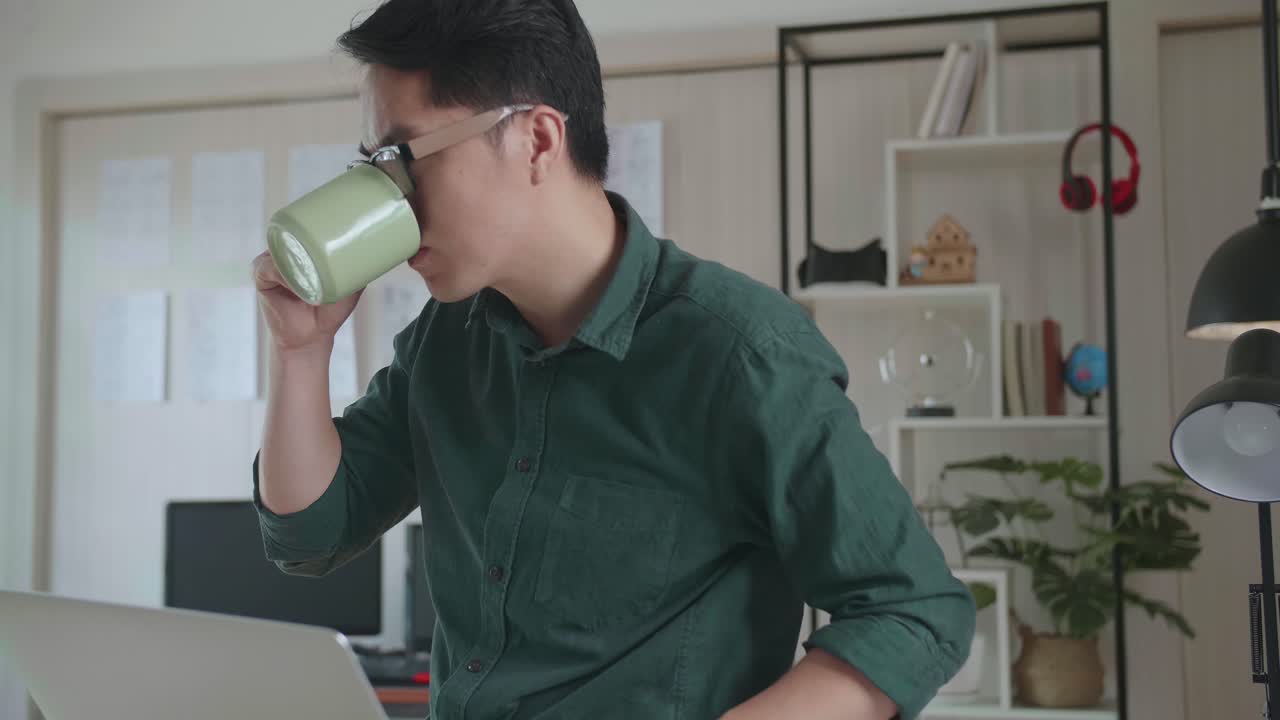 Creative Designer Sits On His Desk Holds Laptop On The Knees Drinks Coffee While Working On The Project. Creative Design And Gaming Content Development Studio