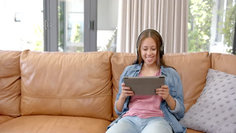sitting on couch, asian woman wearing headphones and using tablet, smiling happily, copy space