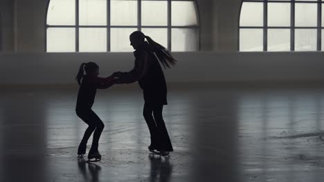 allenamento di pattinaggio artistico. l'allenatrice donna e la sua studentessa stanno girando in cerchio sull'arena di ghiaccio tenendosi per mano. la piccola pattinatrice sta pattinando con il suo allenatore in uno stadio buio. silhouette scure. slow motion