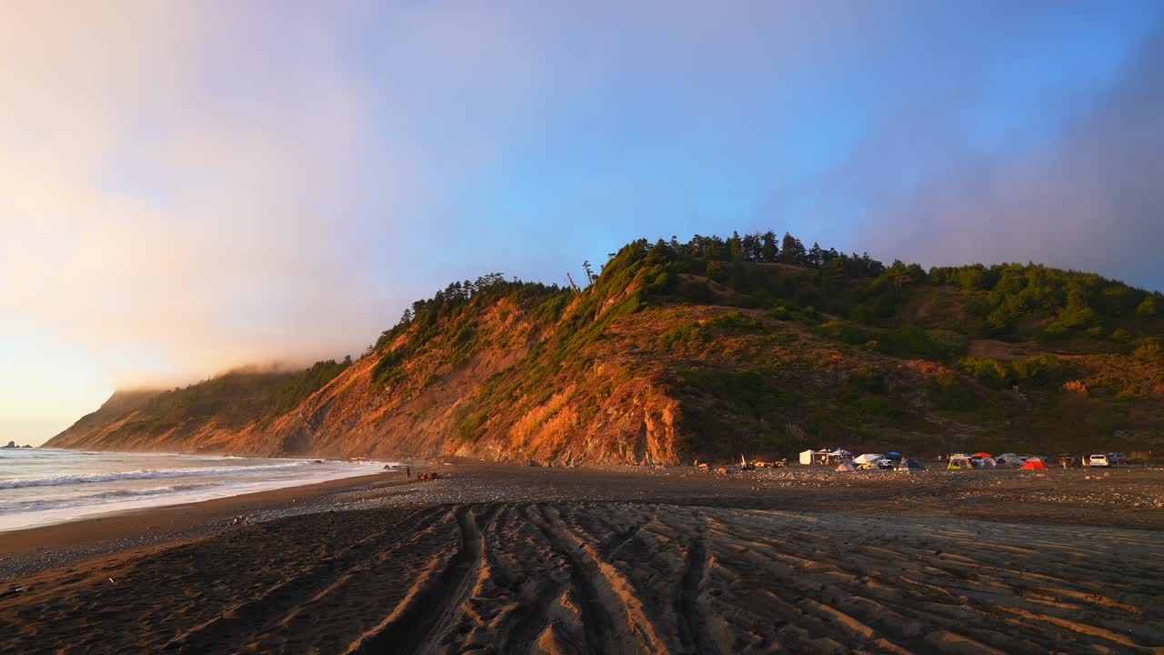 Stunning sunset surf waves USAL Beach campground tents 4wd trucks cars PNW Lost Coast Trail aerial drone California rugged dramatic untouched coastline mist fog clouds nature landscape pan left