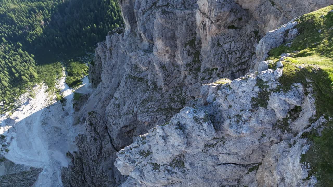 A vertical perspective showcases the Dolomites' sheer rock faces and rugged terrain, contrasting with patches of greenery and the tree-covered valley below