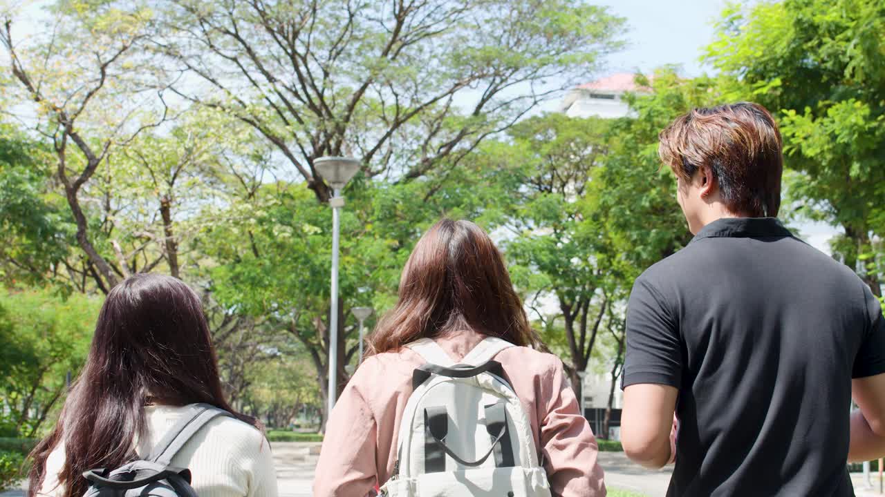 ภาพด้านหลังของนักเรียนสามคนกำลังเดินอยู่กลางแจ้งผ่านวิทยาเขตของมหาวิทยาลัยที่เขียวชอุ่มในประเทศไทย