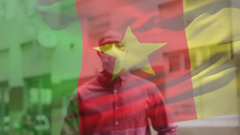 animation of flag of cameroon waving over man wearing face mask during covid 19 pandemic