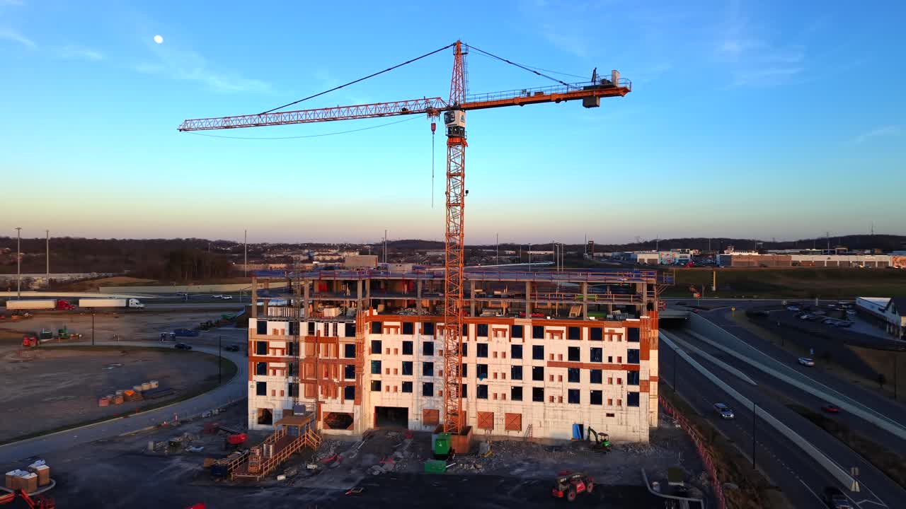 Un progetto di costruzione urbana con una gru imponente e un condominio sotto un cielo notturno sereno, catturato al tramonto con la luna visibile, ripreso con effetto parallasse da drone.