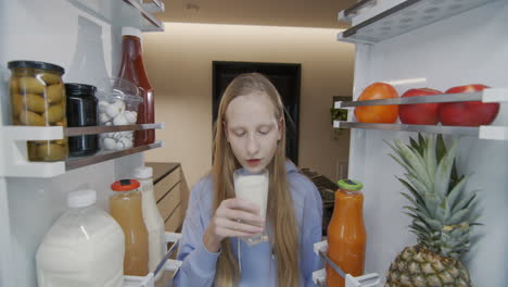 the child opens the refrigerator and drinks milk from a glass. snack on the go