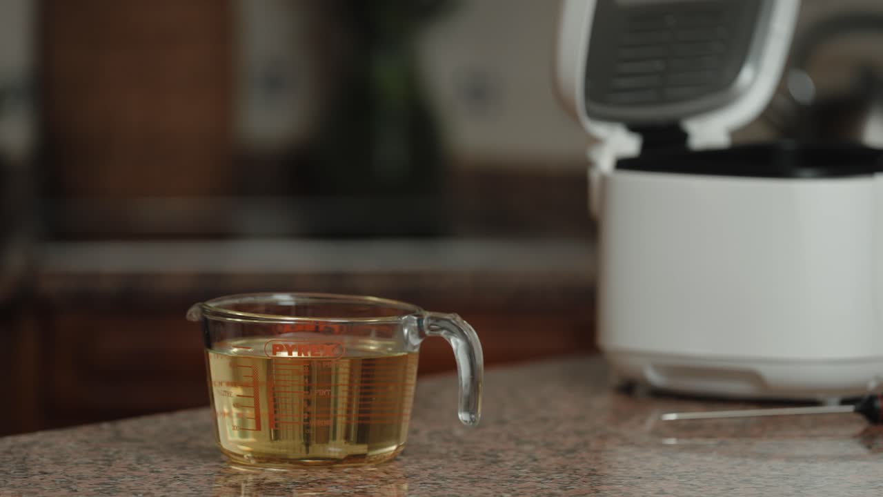 Close up of hand placing glass measuring cup near cooker indoors
