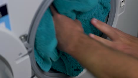 close-up slow motion hands placing cotton towels into front loader washing machine cleaning detergent laundry household chore 4k