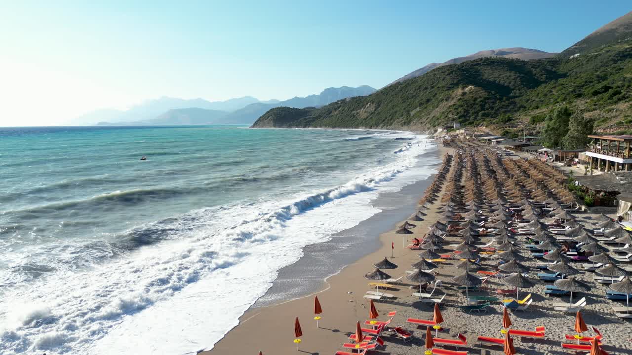 Beautiful beach with sun umbrellas and large waves crashing on the shore with mountains in the background