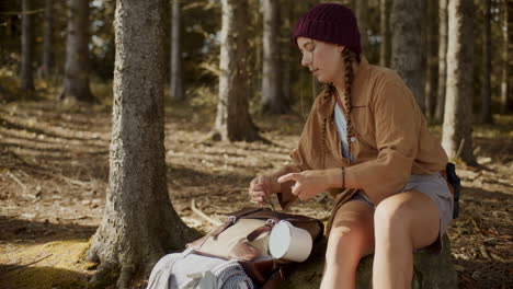 female tourist tying travel mug with backpack in forest