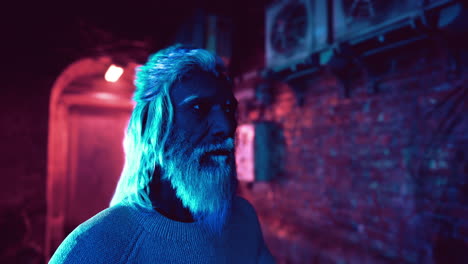 man with long white hair and beard stands in a dark alley lit with blue and red lights