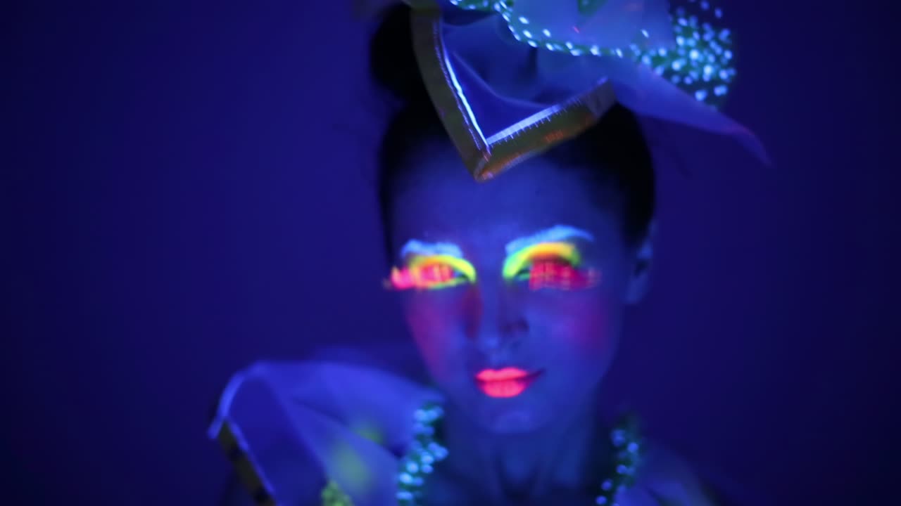 mujer con maquillaje de neón y sombrero en un entorno brillante en la oscuridad