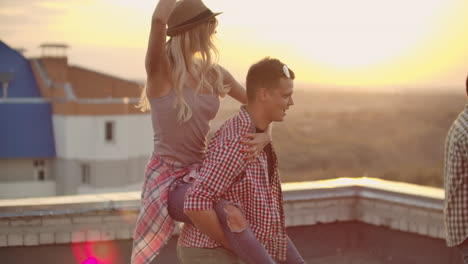 loving couple moves in a dance at a party with friends. a girl sits on her boyfriend's back they are fooling around on the roof.