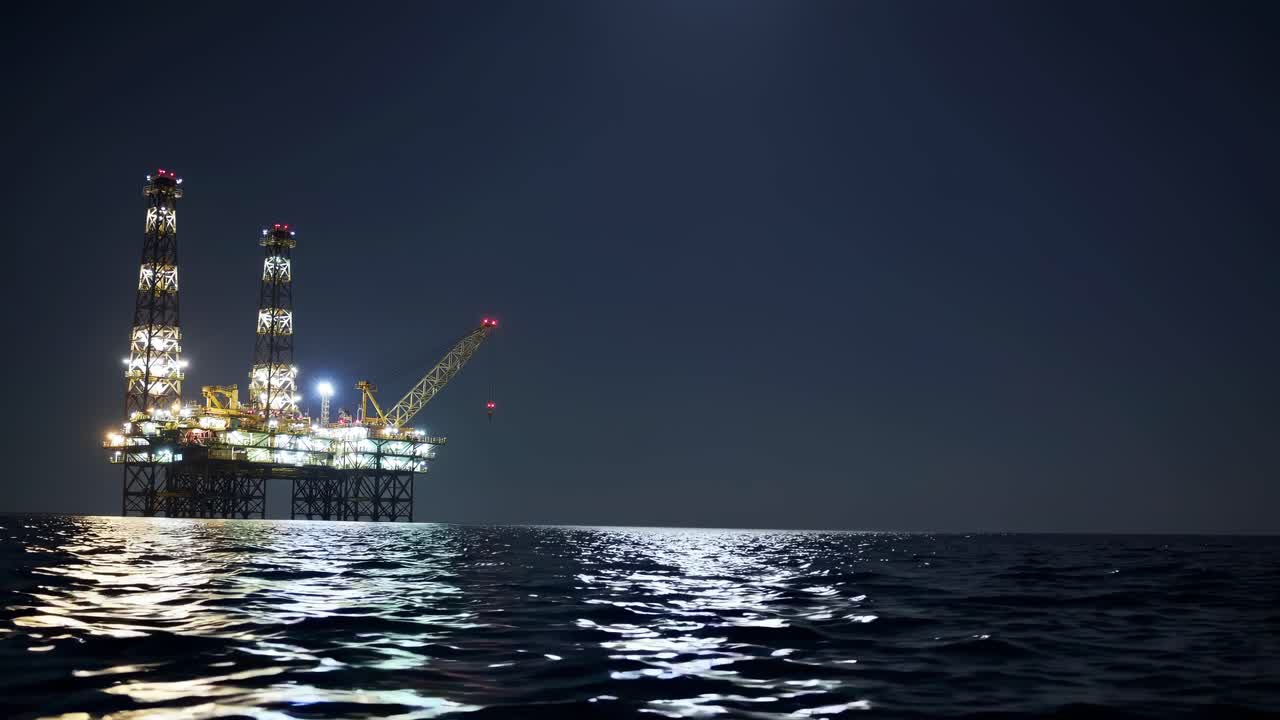En rolig natvideo af en oplyst offshore-olieplatform, der spejler sig i det rolige vand