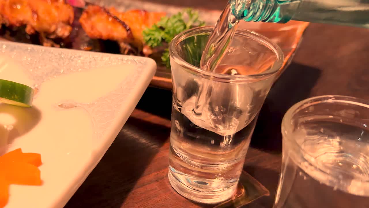 Primo piano di sake limpido versato in un bicchiere accanto a sashimi colorato a Tokyo.
