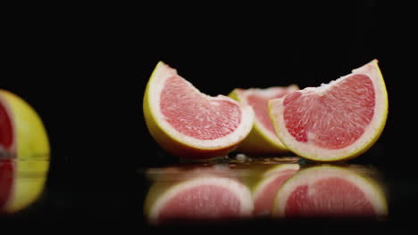 Rote-Saftige-Grapefruitscheiben-Fallen-Auf-Ein-Glas-Mit-Wasserspritzern-In-Zeitlupe-Auf-Dunklem-Hintergrund