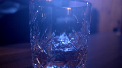 pouring cold whisky into typical glass in dark scenery with blue light