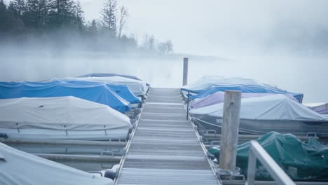 boats docked at pier on misty foggy lake, mountains in background