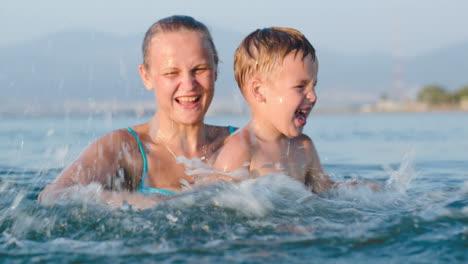 little son and mother fooling in water