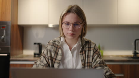 reverse zoom a woman with glasses works remotely from home sitting at a table with a laptop and a felt-tip pen marks the data on the graph. distance learning student at home to perform an assignment