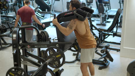 adult brunett man in 30th building leg muscles in standing squat machine at gym