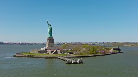 Toma-De-órbita-Aérea:-Estatua-De-La-Libertad-Durante-Un-Día-Soleado-Con-Cielo-Azul-En-Nueva-York,-Estados-Unidos