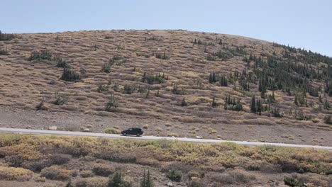 aerial view of the guanella pass highway and a snow covered mount bierstadt while following a vehicle during the fall in colorado. filmed in the rocky mountains with a left trucking movement.
