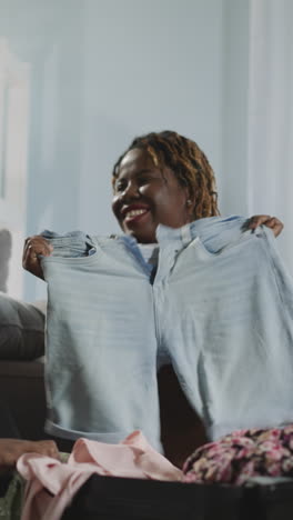 indian and african american women choose clothes to leave in suitcase for summer trip. friends enjoy preparing for vacation on seaside sitting on floor