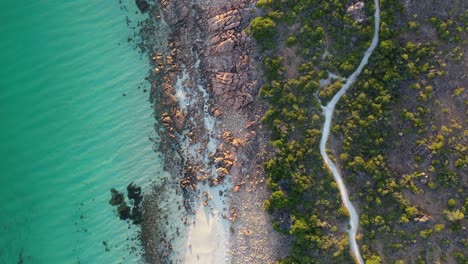 Vista-Aérea-De-Arriba-Hacia-Abajo-De-La-Exótica-Playa-De-Rocas-Del-Castillo-Tropical-Y-La-Carretera-Costera-Entre-árboles-A-La-Luz-Del-Sol-De-La-Hora-Dorada